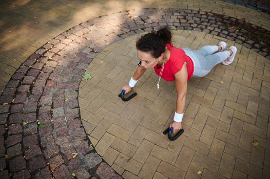 Determined and motivated middle aged African woman of average build in tight sportswear doing push-ups from the floor during a morning workout in a city park on a warm summer day
