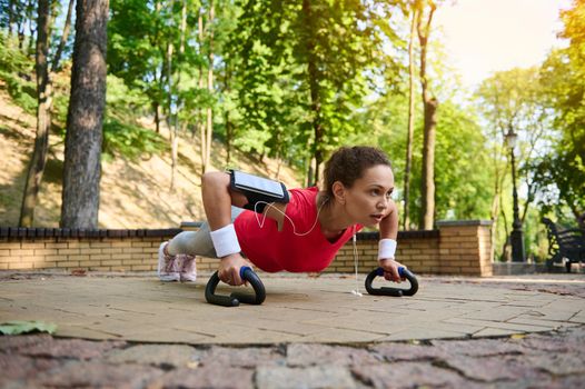 Determined active muscular woman pushing ups from floor while performing full body functional cross training outdoors. Sport, body weight training, weight loss and healthy lifestyle concept