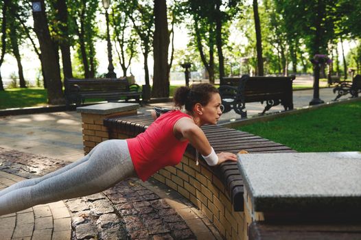Determined motivated middle aged muscular African American athletic woman doing push ups, enjoying morning functional cross workout in city park on a beautiful hot sunny summer day