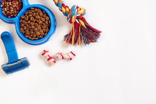 Dog care items, isolated on white background. Dry pet food in bowl, toy and bones. Top view. Copy space. Still life. Flat lay.