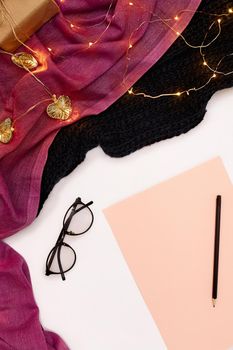 Black glasses, pink paper with new years goals. Scarf and Christmas lights on white background. Top view. Copy space. Still life. Flat lay