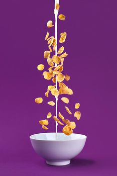 Falling granola with milk splash in bowl. Healthy breakfast ingredients. Flying food on purple background. Still life. Copy space