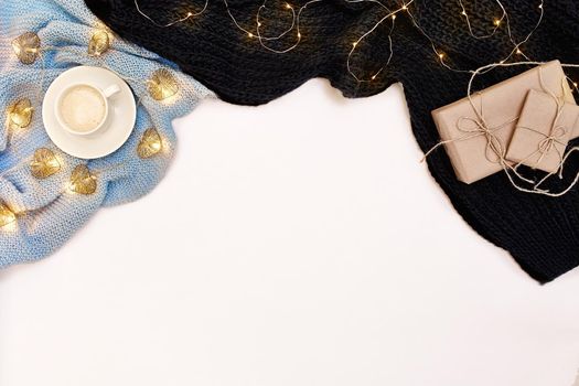 A cup of coffee with warm blue scarf and Christmas garland on white background. Top view. Flat lay. Copy space. Still life