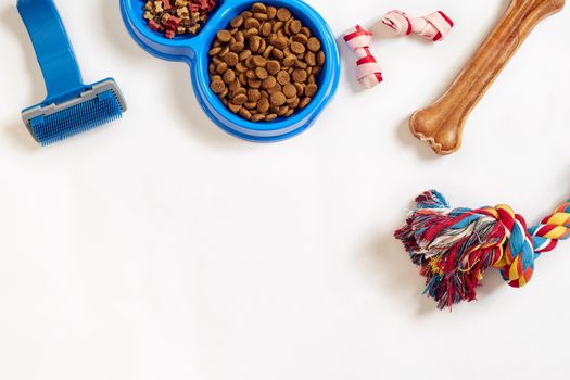 Dog care items, isolated on white background. Dry pet food in bowl, toy and bones. Top view. Copy space. Still life. Flat lay.