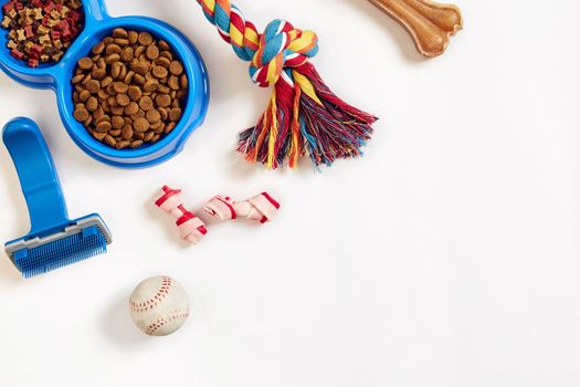 Dog care items, isolated on white background. Dry pet food in bowl, toy and bones. Top view. Copy space. Still life. Flat lay.