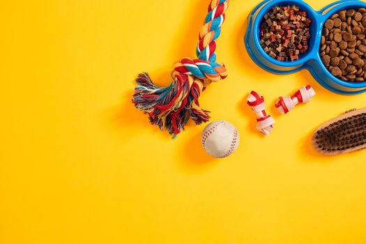 Toys -multi coloured rope, ball and dry food. Accessories for play on yellow background top view. Still life. Copy space. Flat lay