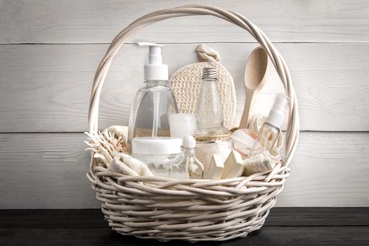 Composition of cosmetic bottles and soap in basket, on white wooden background. Still life. Copy space. SPA set