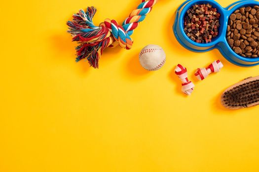 Toys -multi coloured rope, ball and dry food. Accessories for play on yellow background top view. Still life. Copy space. Flat lay