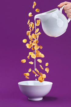 Falling granola with milk splash from dipper. Healthy breakfast ingredients. Flying food on purple background. Still life. Copy space