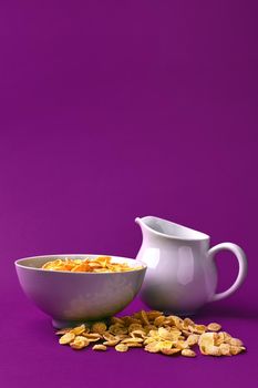 Bowl with corn flakes, jug of milk on purple background. oncept of a healthy breakfast. Copy space. Still life. Flat lay