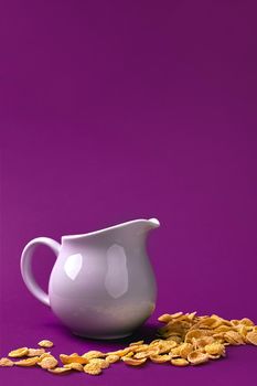 Close-up view of jug with milk and crunchy corn flakes on purple background. Still life. Copy space.