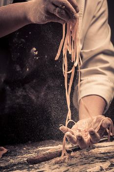 The chef makes fresh spaghetti from scratch. Wooden table. Photo in brown tones. Kitchen.