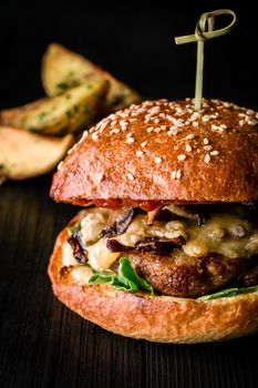 Cheese burger with grilled meat, cheese, tomato and potatoes on dark wooden surface. Fast food template. Real photo. Ideal for advertisement. Close-up. Still life hamburger