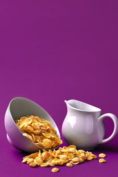 Bowl with corn flakes, jug of milk on purple background. oncept of a healthy breakfast. Copy space. Still life. Flat lay