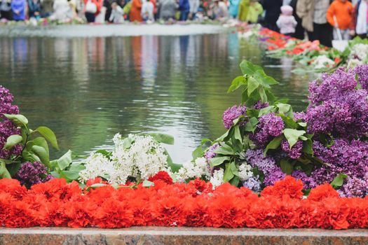 Red carnations and lilacs on a marble military memorial near water