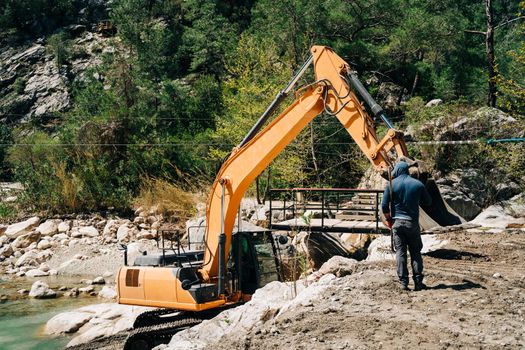 Heavy machinery dragline excavator digging ground in the mountain canyon. Digger ditcher working on a gold mine in the mountains. Mining equipment.