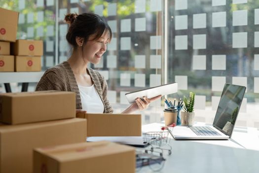 Sell online, Young asian woman checking order and customer's details and addresses on laptop or box in order to prepare for shipping according to the information, Online shopping SME entrepreneur.