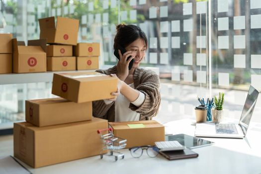 Small business entrepreneur SME freelance woman using phone call receive from customer checking product on stock at home office, online marketing packaging delivery box, SME e-commerce concept.