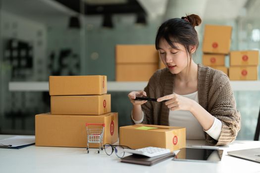 Young asian businesswoman owner packing and take a photo on cardboard box, Young Owner Woman Start up for Business Online. People with online shopping SME entrepreneur or freelance working concept.