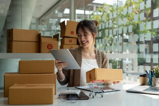 Sell online, Young asian woman checking order and customer's details and addresses on laptop or box in order to prepare for shipping according to the information, Online shopping SME entrepreneur.
