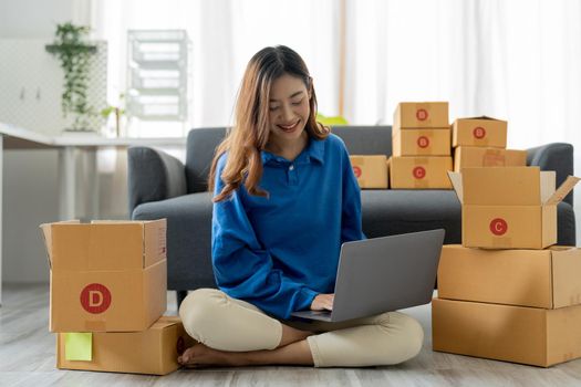Startup SME small business entrepreneur, holding card box standing at her home office. Beautiful success Asian businesswoman online marketing, SME preparing package parcel delivery to her customer.