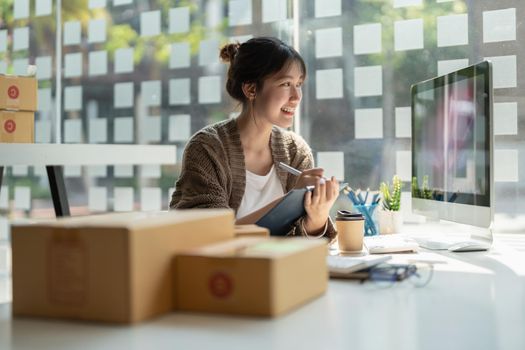 Sell online, Young asian woman checking order and customer's details and addresses on laptop or box in order to prepare for shipping according to the information, Online shopping SME entrepreneur.
