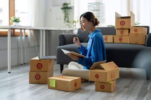 Sell online, Young asian woman checking order and customer's details and addresses on laptop or box in order to prepare for shipping according to the information, Online shopping SME entrepreneur.