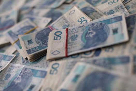 A file of cash bound with a rubber band lies on top of loosely and randomly distributed fifty dollar paper bills.