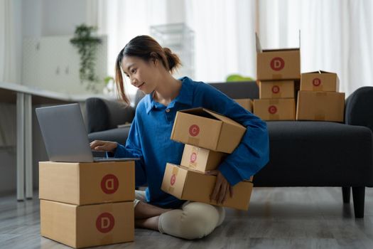 Attractive Asian woman online working in office desk use laptop computer, online marketing packaging box delivery, SME e-commerce concept.