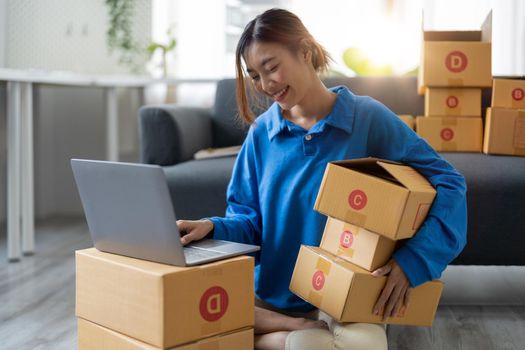 Attractive Asian woman online working in office desk use laptop computer, online marketing packaging box delivery, SME e-commerce concept.
