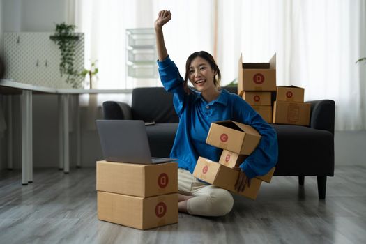 Attractive Asian woman online working in office desk use laptop computer, online marketing packaging box delivery, SME e-commerce concept.