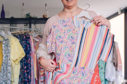 cropped shot of a woman picking up and buying clothes in a fashion shop. concept of shopping.concept of leisure. natural light from the shop window, sun rays, display with clothes, clothes rack, shop window, clothes, vertical