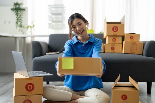 Young Asian Woman holding parcel box for delivery to customer by logistic service. small business entrepreneur SME distribution warehouse. small owner home office and Online marketing product theme.