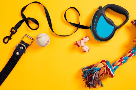 Toys -multi coloured rope, ball, leather leash and bone. Accessories for play and training on yellow background top view. Still life. Copy space. Flat lay