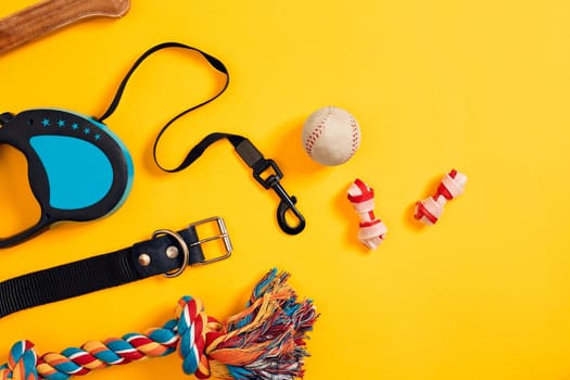 Toys -multi coloured rope, ball, leather leash and bone. Accessories for play and training on yellow background top view. Still life. Copy space. Flat lay