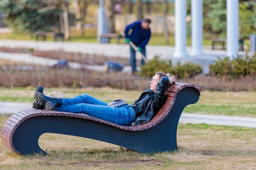 The girl lies on a sun lounger in the park with her eyes closed, hands behind her head. The girl is resting and relaxing. Moscow Russia April 23, 2022.