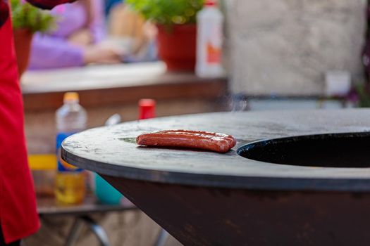 Two sausages are warmed up on a round stove in a street cafe.