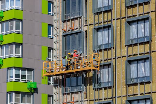 Male builders work on the facade of the building in a suspended cradle. Construction works. Moscow Russia April 14, 2022