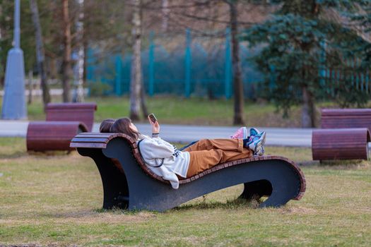 Two girls lie on a sun lounger in the park, look at the phone after spending their free time.