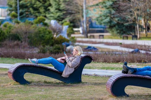 A woman lies on a sun lounger in the park, looks at the phone, spends her free time. Moscow Russia April 23, 2022.