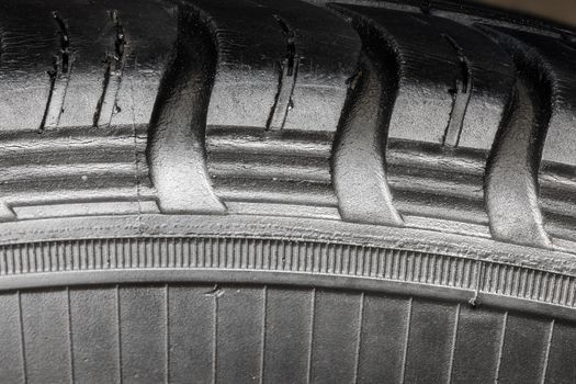 Old worn black tire with many large cracks in the car wheel. High magnification macro view.
