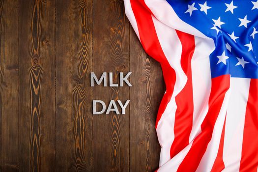 the word MLK day laid with silver metal letters on wooden surface with crumpled USA flag at right side in directly above high angle view. MLK means Martin Luther King Jr.
