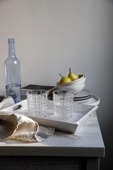 A blue transparent water bottle and two ribbed glasses on a white wooden tray on the kitchen table.
