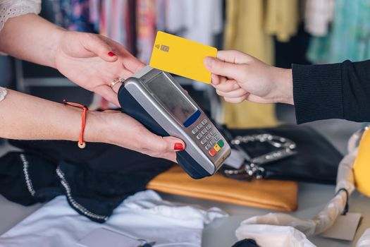 saleswoman cashing with credit card. woman paying with contactless. concept of shopping. close-up. natural light, horizontal view, young woman shopping, mature woman business owner, close-up