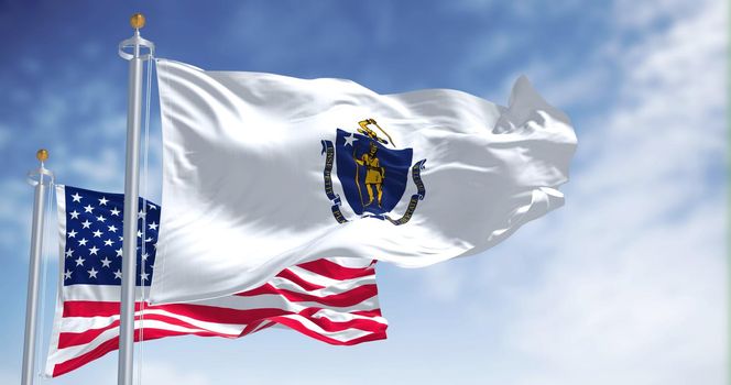 The Massachusetts state flag waving along with the national flag of the United States of America. In the background there is a clear sky. Massachusetts is a state in the New England region of the United States