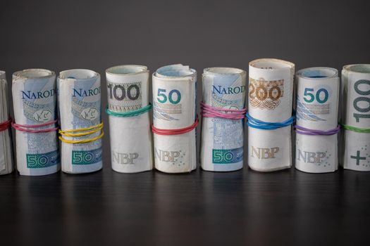 A collection of multiple denominations of Polish national currency rolled up and compressed with a rubber band.