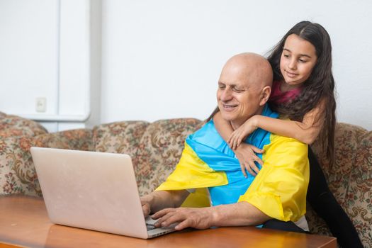 Grandfather and granddaughter with laptop and flag of Ukraine.