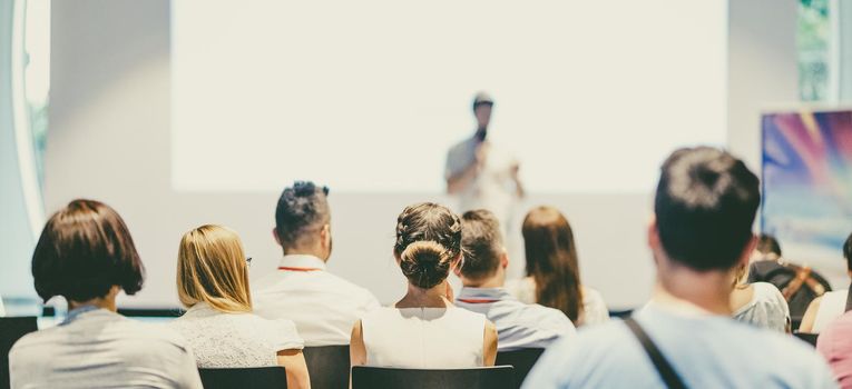 Speaker giving a talk in conference hall at business event. Audience at the conference hall. Business and Entrepreneurship concept. Focus on unrecognizable people in audience.