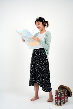 Positive smiling young asian female tourist searches for inspiring places, holds paper map, finds new sightseeing for discovering, wears round spectacles, isolated on white studio wall.