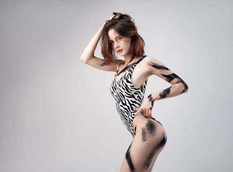 the slender girl in a spotted bodysuit swimwear painted with spots of black paint on a white background